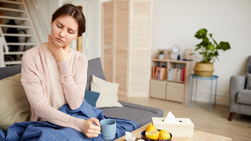 Young Woman With Sore Throat Sitting on Grey Sofa